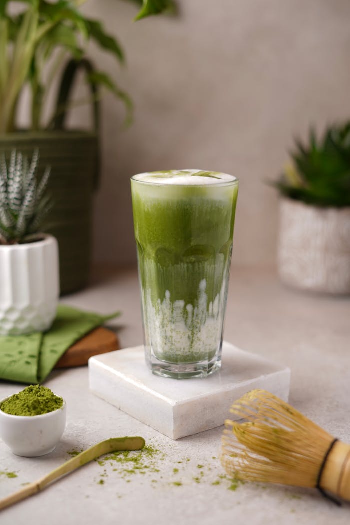 menu-01 Green matcha latte in a tall glass with tools and plants, calm setting.